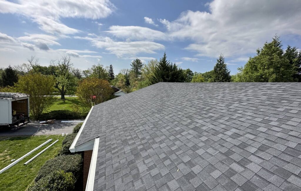 Gray shingle roof on a home, with blue sky and trees in background.